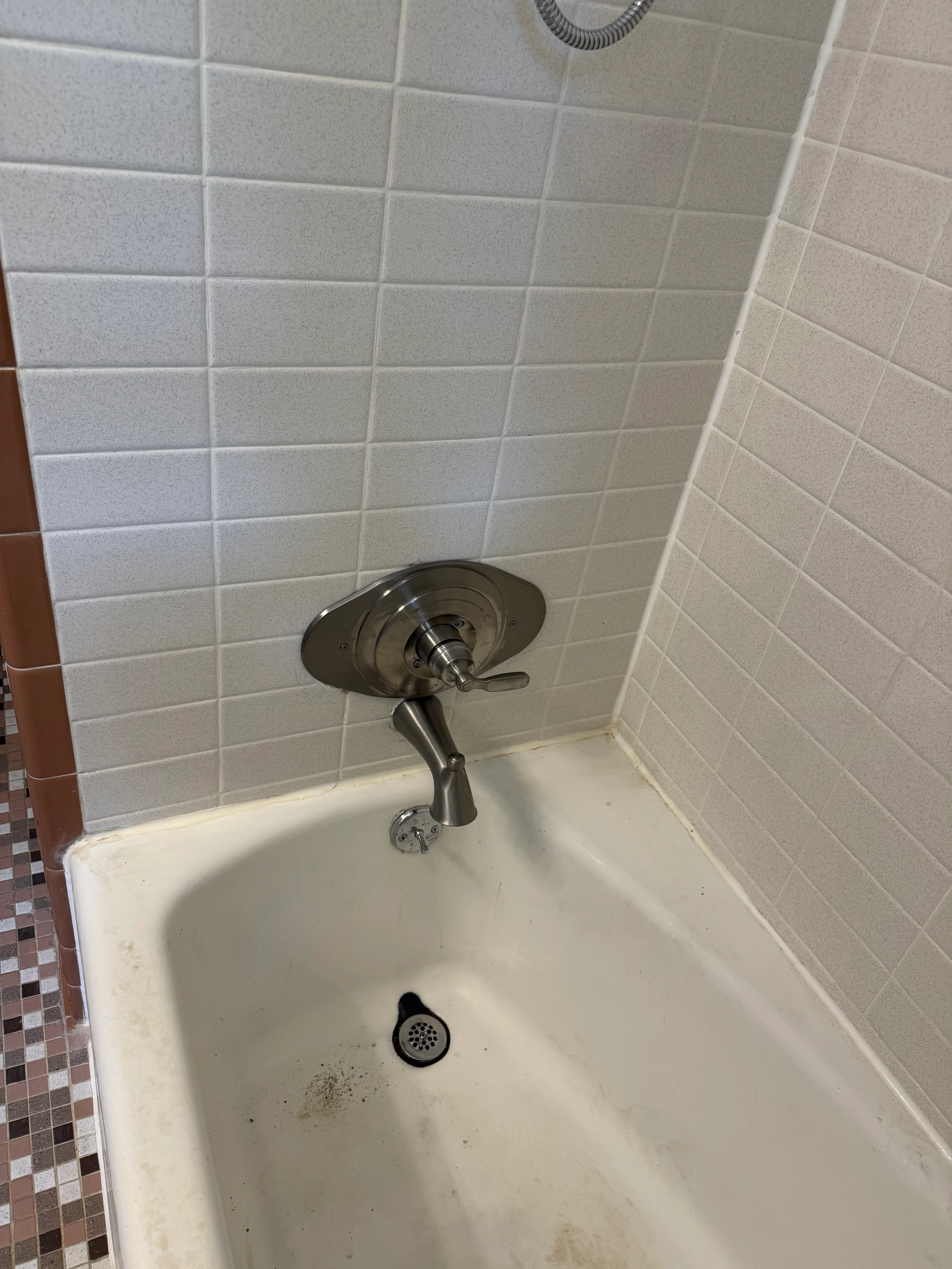 Close-up of newly installed chrome shower valve trim with handle in a tile shower enclosure