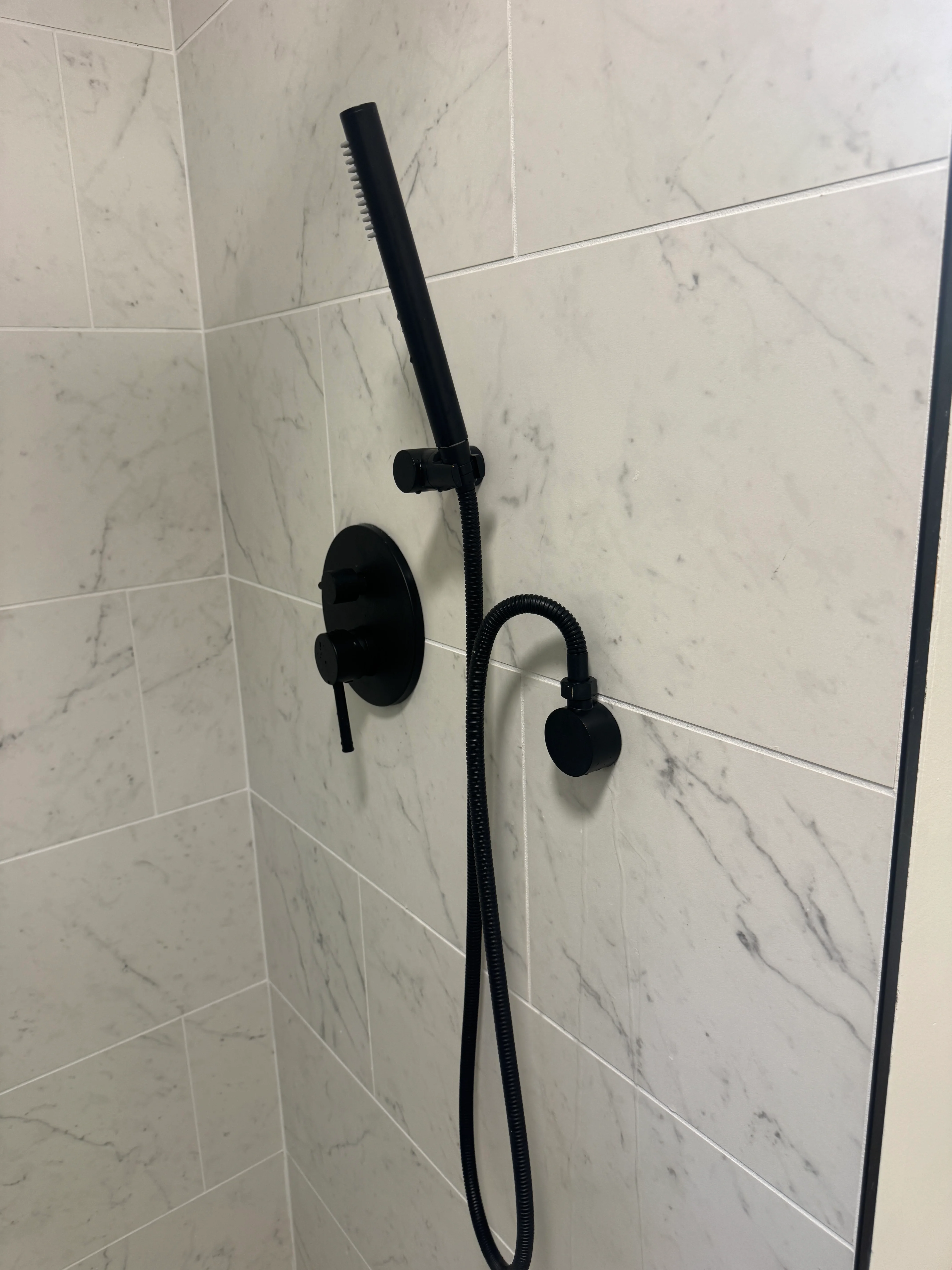 Newly installed matte black handheld showerhead mounted on bathroom wall with chrome trim ring