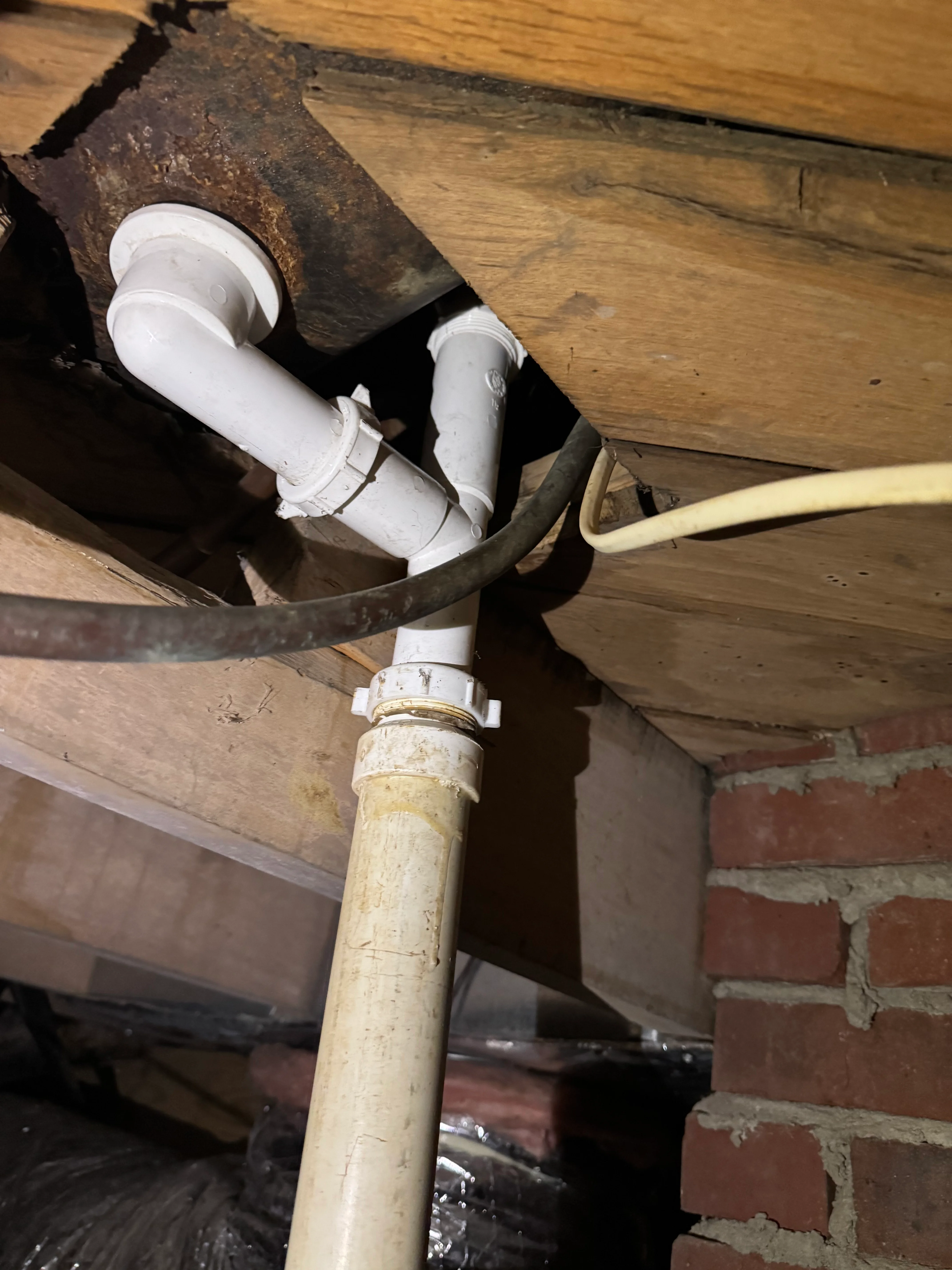 White PVC drain pipes installed in crawl space with brick foundation visible